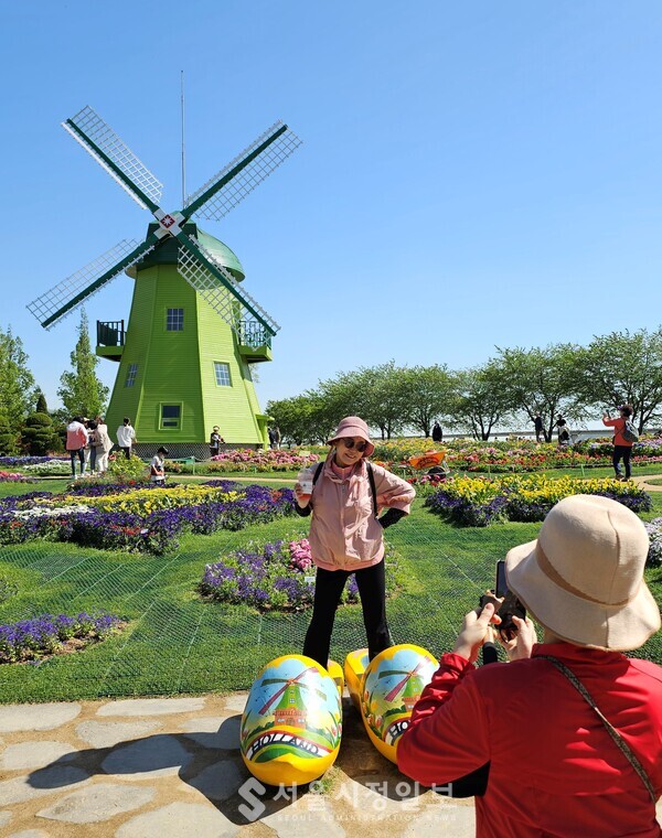 네델란드 정원의 풍차 앞에서 관람객이 미소를 지으며 사진을 찍고 있다.